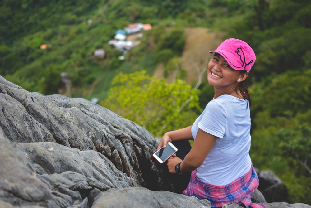 woman sitting on rock cliff near trees at daytime