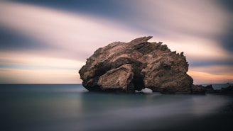 rock formation on body of water under golden hour