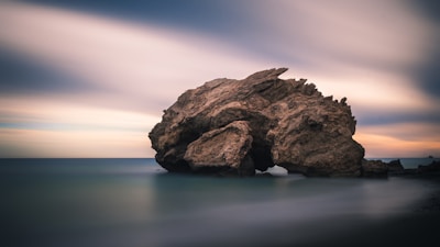 rock formation on body of water under golden hour