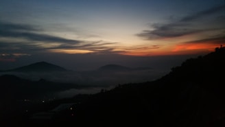 A serene landscape featuring dark, misty mountains under a twilight sky, evoking a sense of mystery and tranquility.