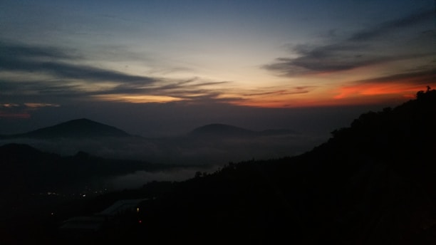 A serene landscape featuring dark, misty mountains under a twilight sky, evoking a sense of mystery and tranquility.