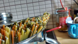 Close-up of a sleek black box with golden accents filled with steaming, colorful pasta.