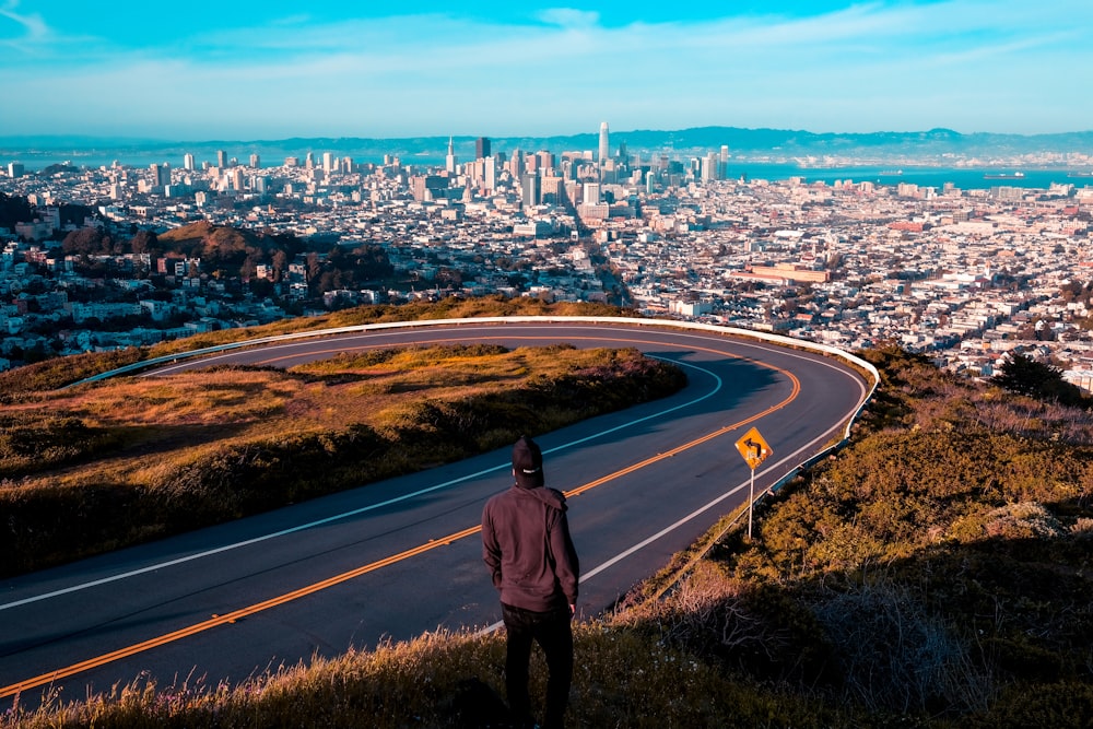 man standing near road looking at city buildings