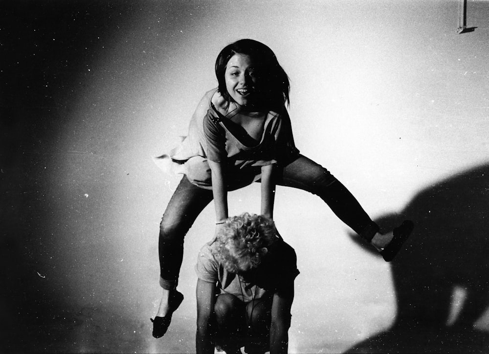 woman jumping on other person's back in grayscale photography