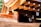A detailed view of wooden architectural elements featuring smooth, curved surfaces and precisely cut beams. Copper or bronze metalwork adds a reflective quality to the structure, with sunlight enhancing the warm tones. The craftsmanship highlights traditional construction techniques.