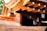 A detailed view of wooden architectural elements featuring smooth, curved surfaces and precisely cut beams. Copper or bronze metalwork adds a reflective quality to the structure, with sunlight enhancing the warm tones. The craftsmanship highlights traditional construction techniques.