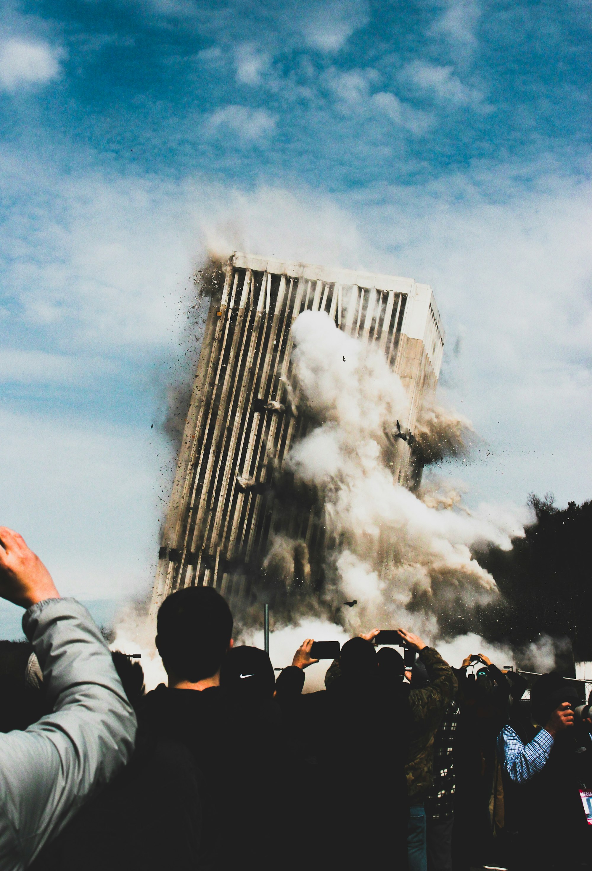 A group of people watch and record a building being imploded.