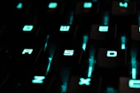 Mechanical keyboard with vibrant cyan backlighting, keys reflecting a futuristic workspace ambiance.