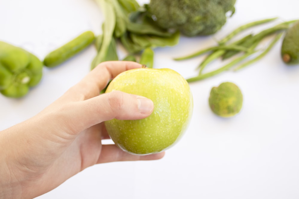 person's hand holding green apple