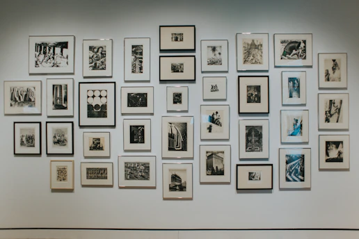 A minimalist art gallery wall featuring black, white, gray, and red accents with framed paintings and photographs.