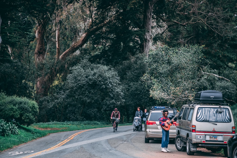 two vehicle park beside the road with people passing by surrounded with trees