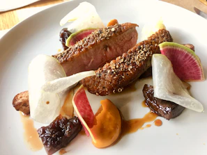 Artfully plated Asian fusion dish featuring seared duck breast with a glossy ginger glaze and colorful vegetable medley