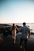 A candid moment of the couple walking barefoot on a sandy beach at sunset.