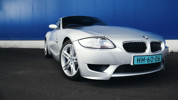 Side view of a sleek silver grand touring car with shiny rims against a dark wall
