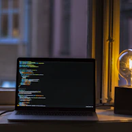 Close-up of hands typing code on a keyboard, illuminated by a warm mustard yellow desk lamp.