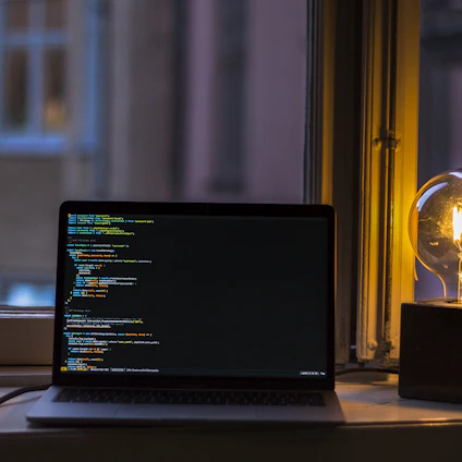 A cozy nighttime developer workspace with a glowing laptop screen showing lines of code.
