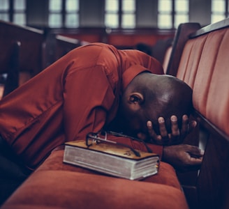 man in orange top beside eyeglasses on brown book