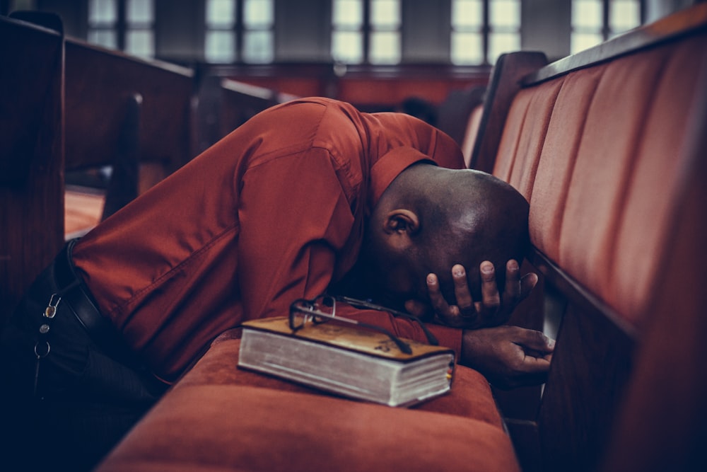 man in orange top beside eyeglasses on brown book