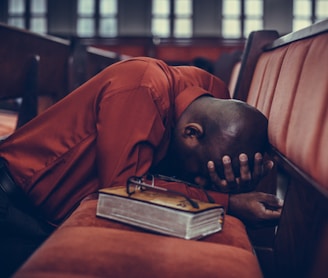 man in orange top beside eyeglasses on brown book