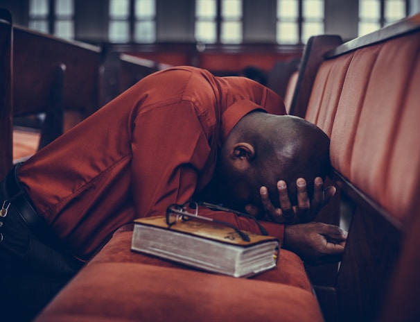 man in orange top beside eyeglasses on brown book