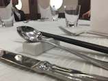 Elegant argentia silverware clip securing knives and spoons wrapped in a linen napkin at a dinner setting.