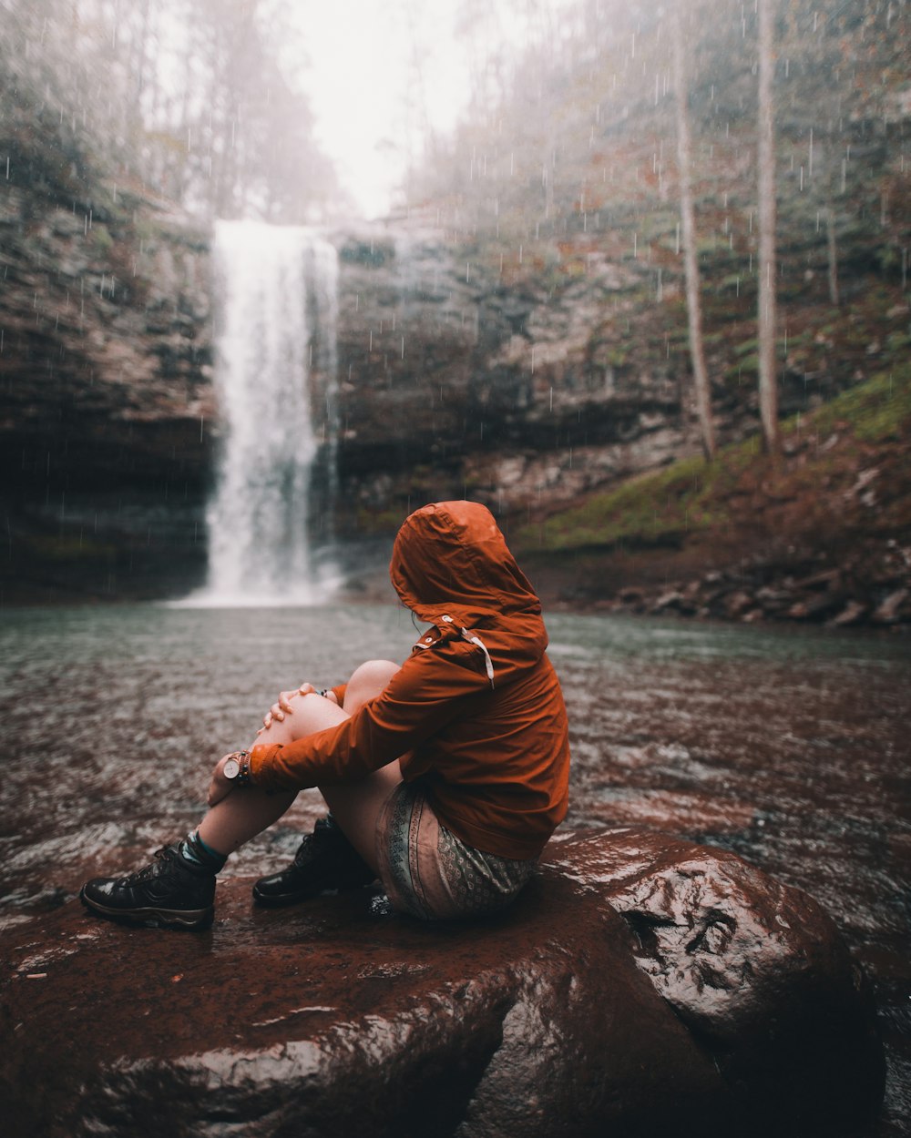Frau sitzt tagsüber auf dem Felsen mit Wasserfall in der Ferne