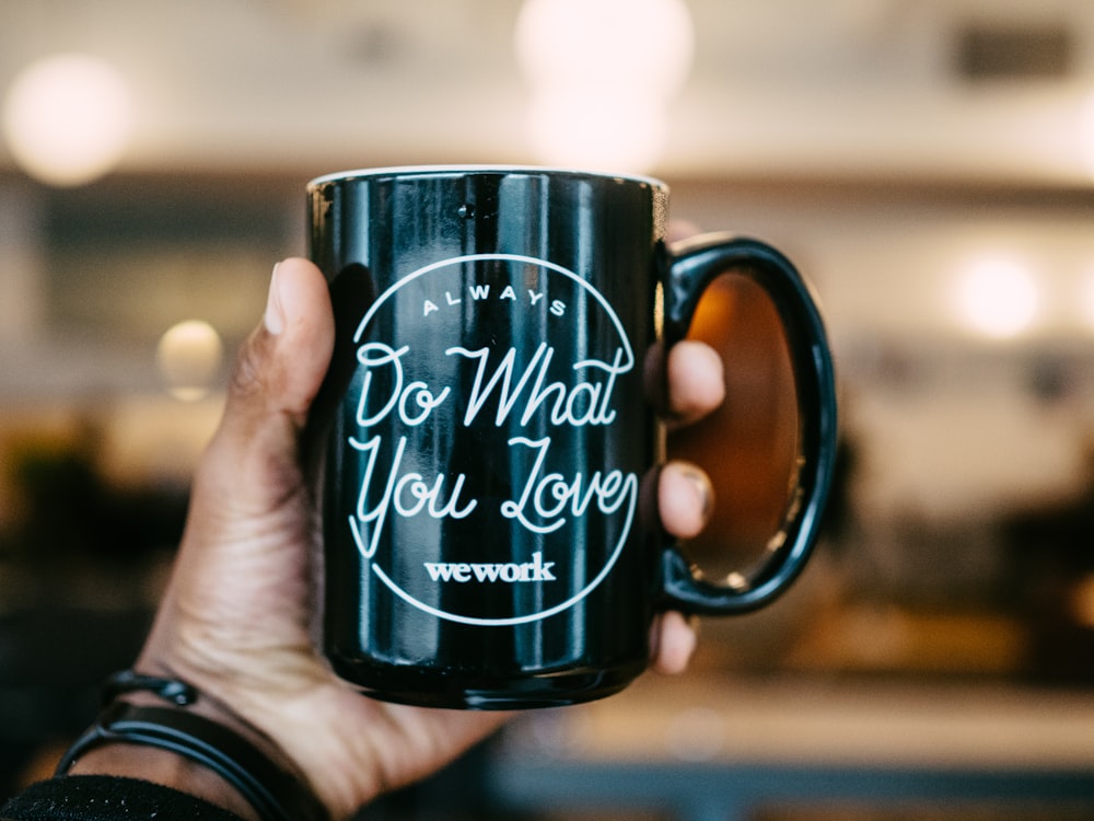 shallow focus photo person holding black ceramic mug