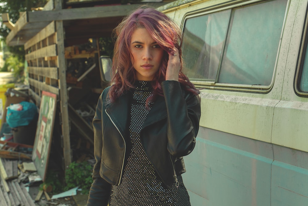 photography of woman in black jacket holding her hair standing beside van