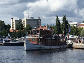 A traditional wooden sailing vessel docked along a bustling coastal settlement.