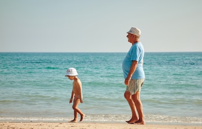 man in blue shirt standing on seashore near boy in white hat