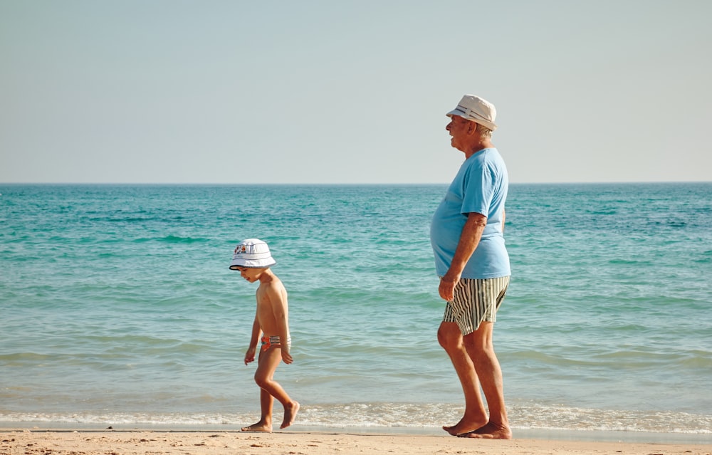 파란 셔츠를 입은 남자가 흰 모자를 쓴 소년 근처 해변에 서 있다