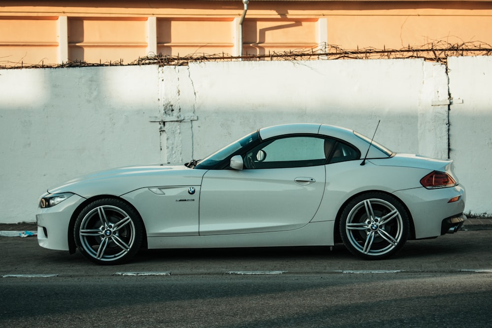 white coupe parked beside white concrete wall