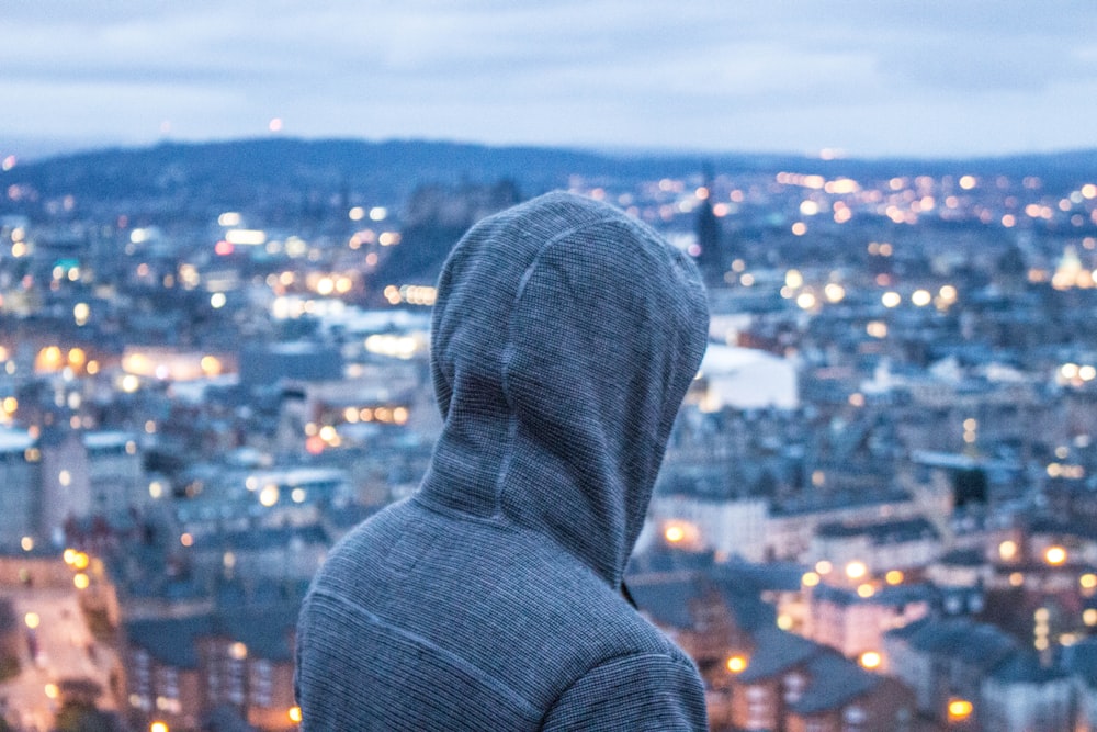 Persona che indossa una felpa grigia con cappuccio in piedi mentre affronta la vista aerea della città