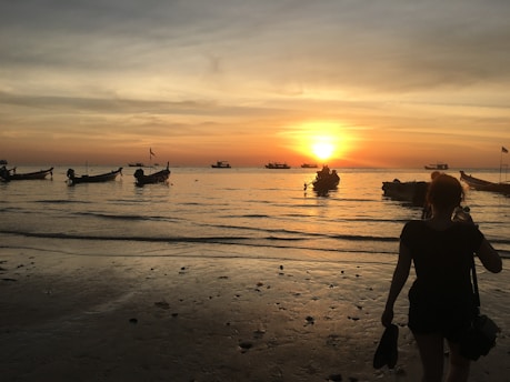 A serene sunset over the calm waters of Muro Alto beach with colorful boats anchored near the shore.
