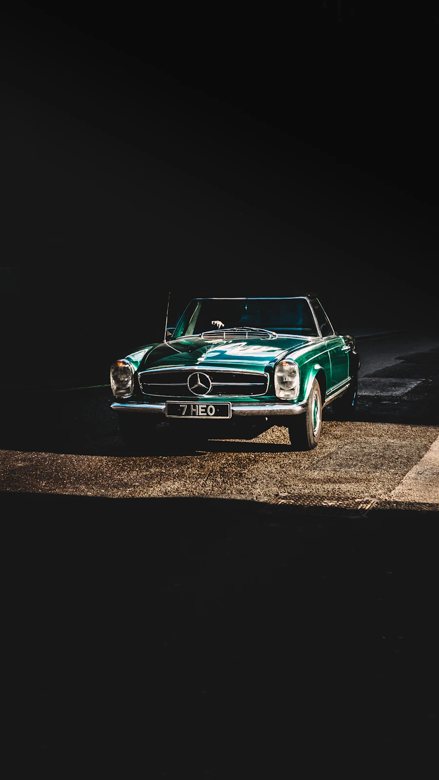 A green classic roadster lit against a dark background