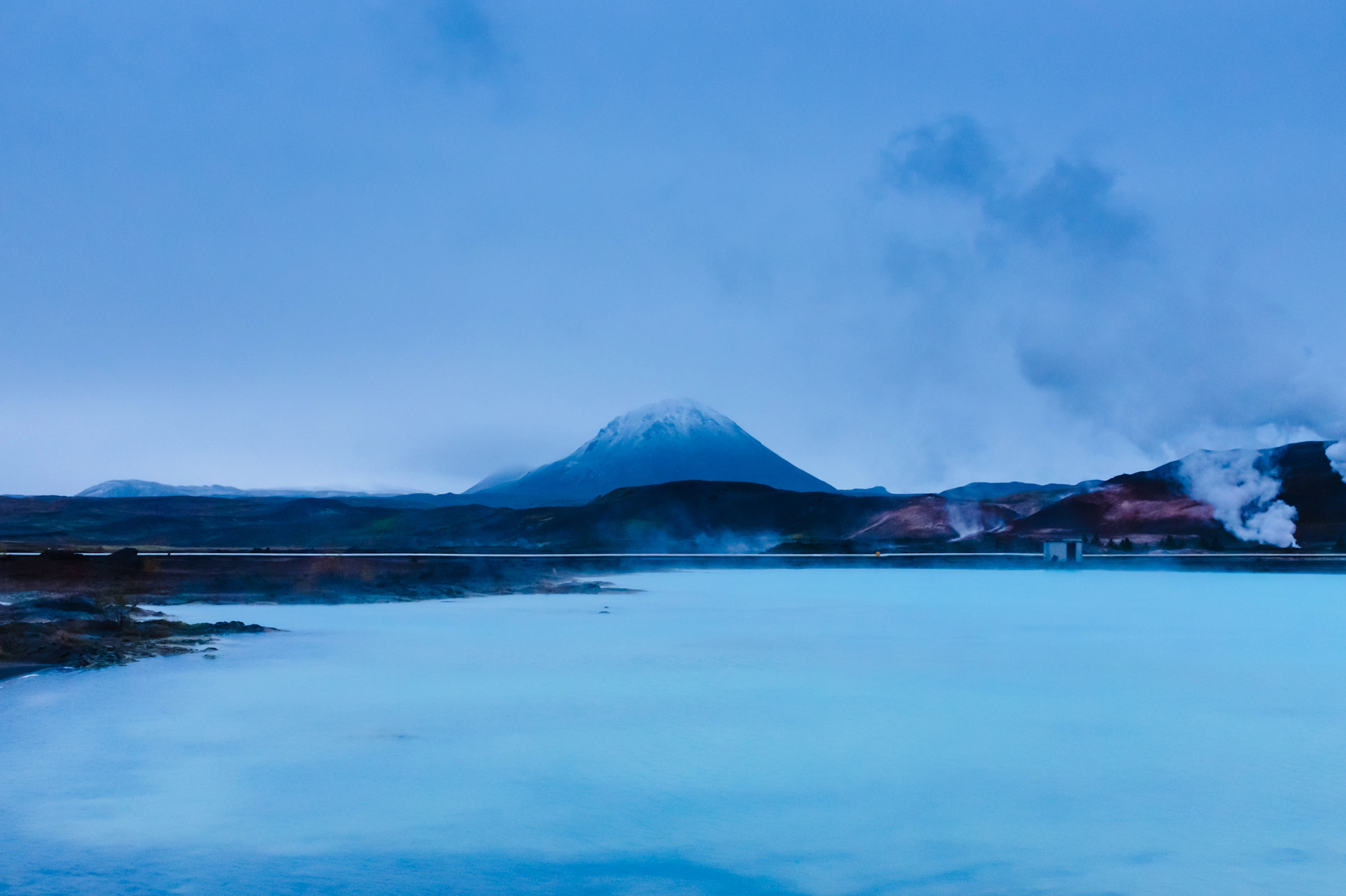 Milky-blue geothermal water and rising steam in the Mývatn area, with a mountain behind