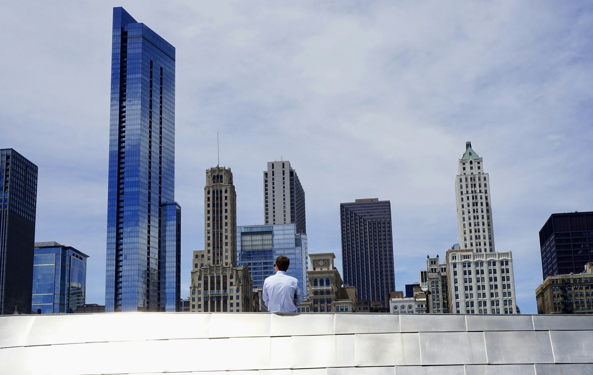 photography of man sitting on roof while looking at city buildings