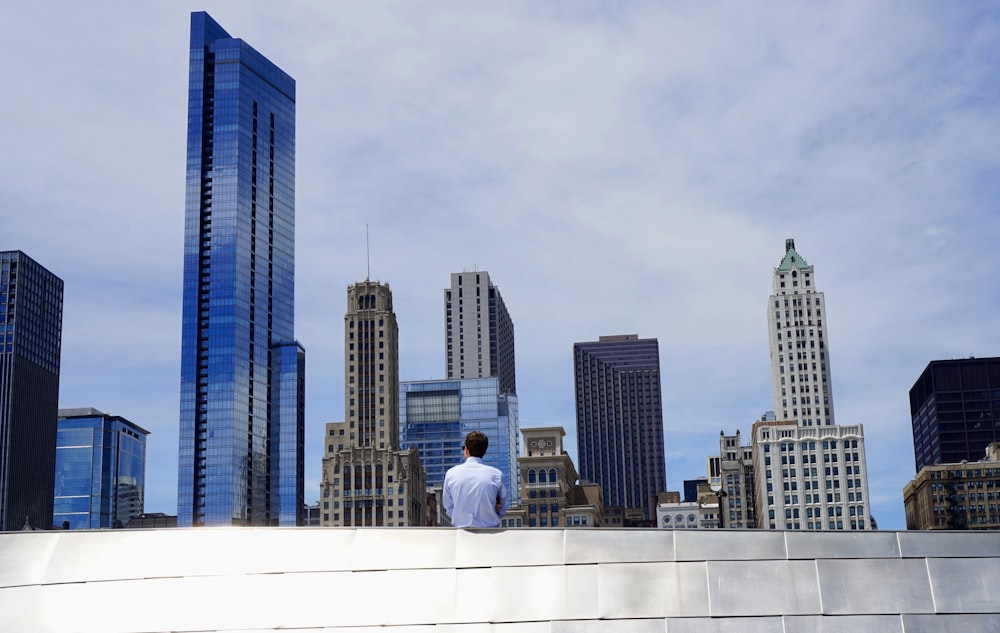 photography of man sitting on roof while looking at city buildings