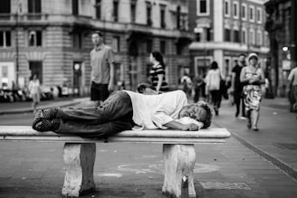 man sleeping on bench in the middle of the street