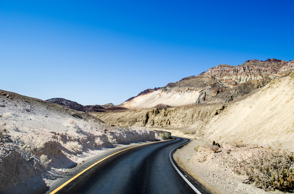 empty roadway between mountains under blue sky at daytime
