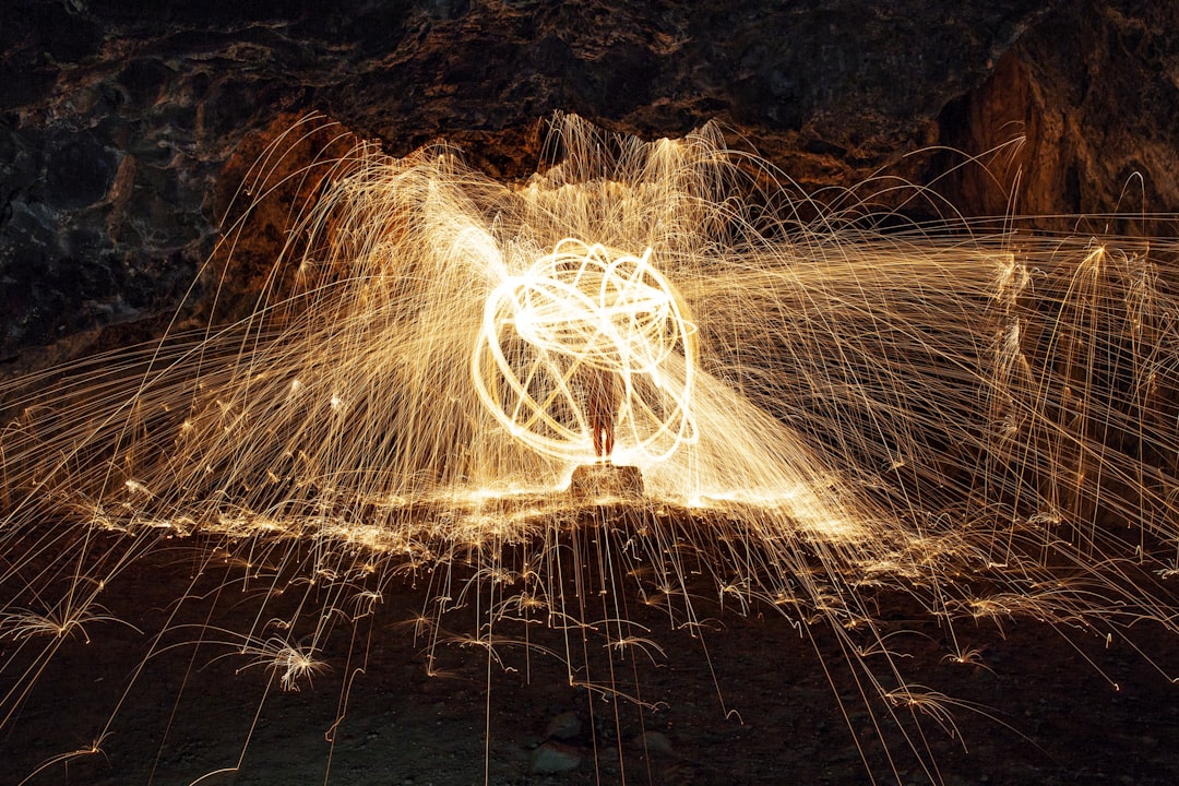 a person standing in a field with a light painting on it, This shot was taken inside of Kaneana Cave in Hawaii. Weaved some steel wool into a whisk, tied it to the end of a camera strap, lit it on fire, then swung it around.<p></figure>We played with different shapes and angles, but I think this one came out the best. My favorite part of this photo is how you can see the person’s legs in the middle of the ball. It’s almost like he’s stuck inside of this spherical cage.