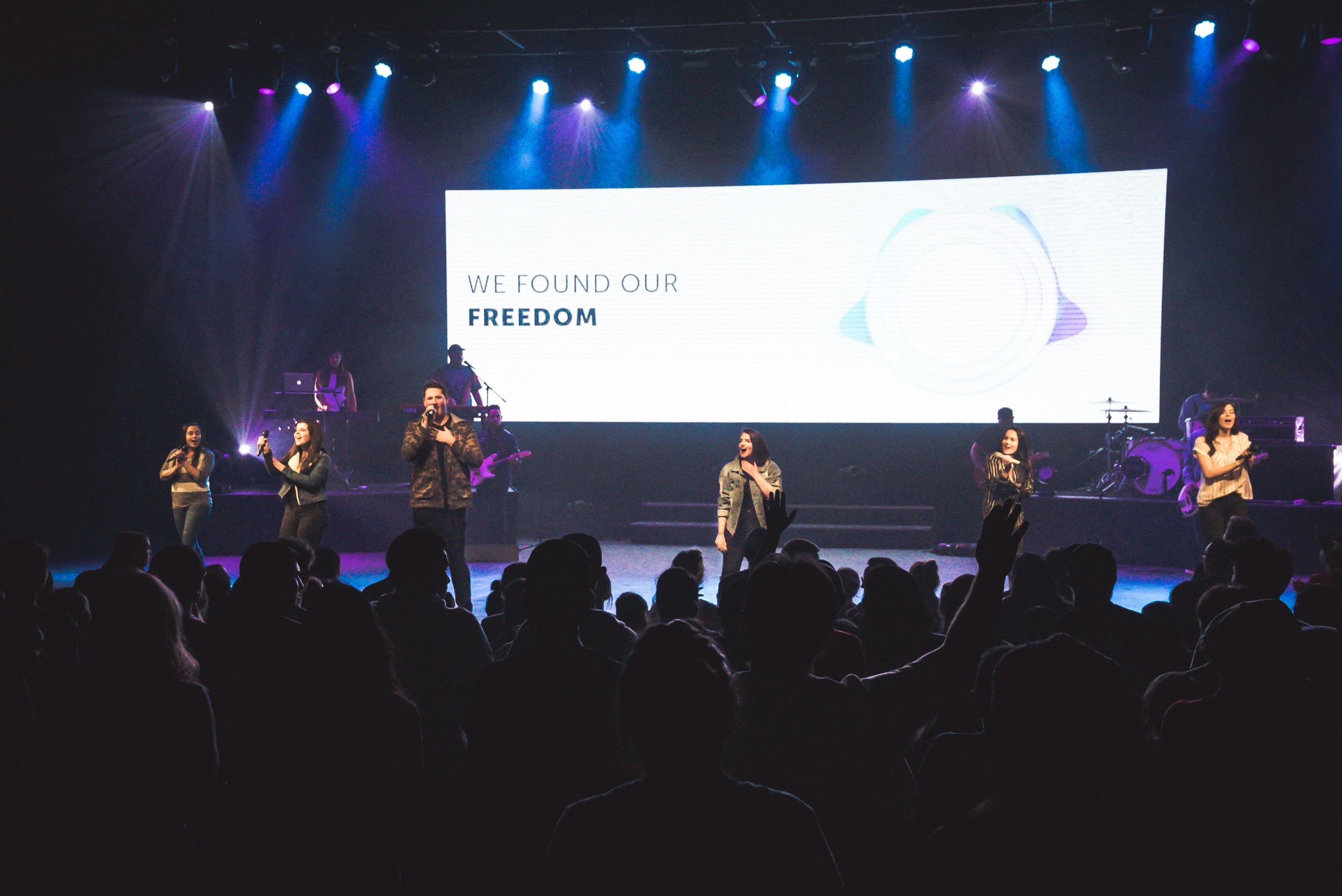 Performers sing on stage in front of a large screen.