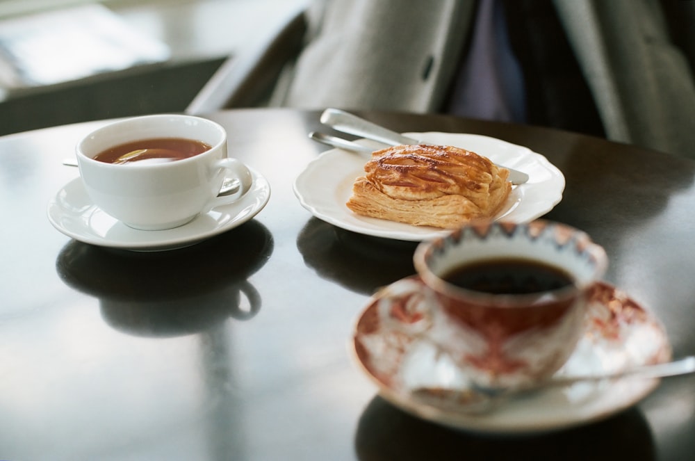 Pan en un plato de cerámica cerca de una taza de té de cerámica blanca llena de café