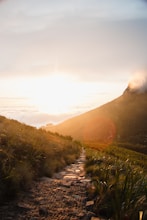 sun shining over mountain ranges with grass field