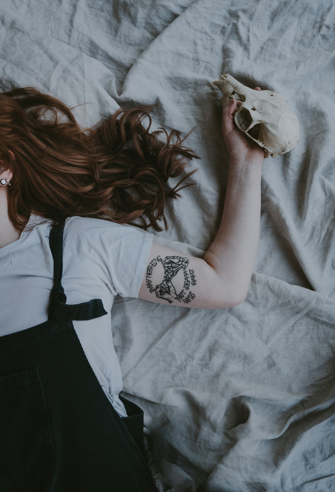 woman laying on gray bed with left arm tattoo