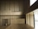Spacious interior with wooden paneling covering the walls and floors, creating a minimalist and modern aesthetic. Large windows on the right side allow natural light to brighten the space. The design is sleek with clean lines, and there are several chairs positioned in an upper section.