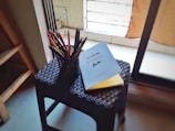 A sunlit workspace with art supplies and a notebook open on a wooden table.