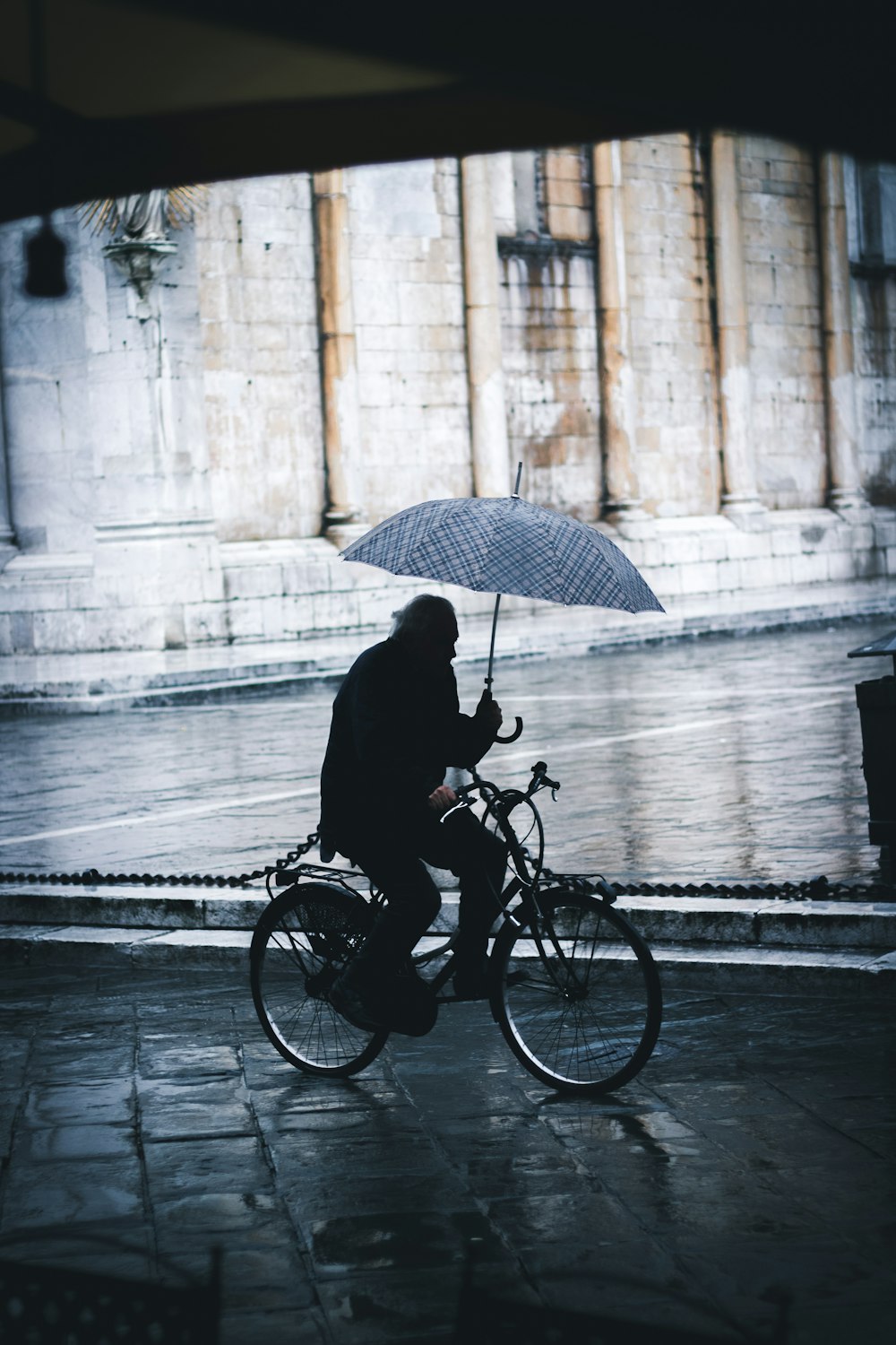 man riding bicycle while holding umbrella near street