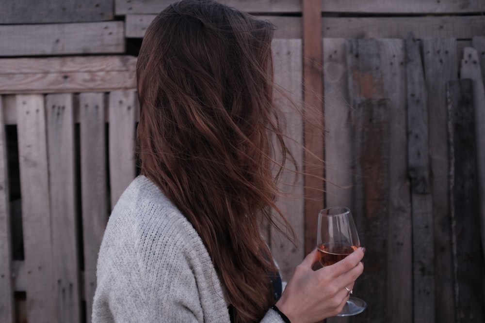 woman holding wine glass standing in front of wooden fence