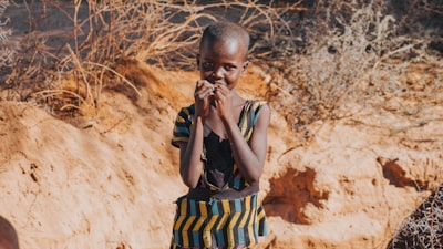 girl blue and yellow striped sleeveless dress standing near green grass kenya teams background